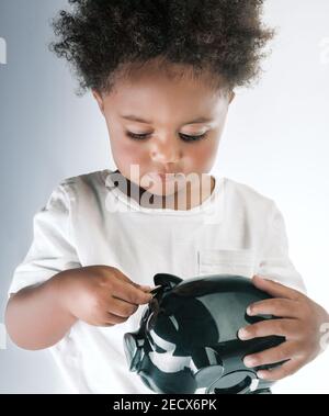 Porträt eines niedlichen kleinen afroamerikanischen Jungen mit Schweinebank in den Händen. Isoliert über leerem grauweißen Hintergrund. Investition in die Zukunft. Stockfoto