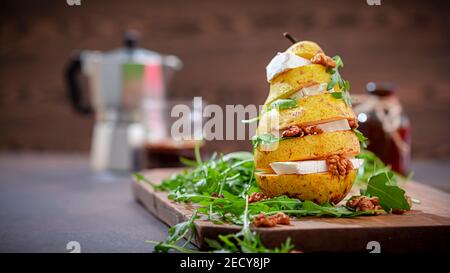 Turmbirne mit Käse, Walnüssen, Rucola, mit Honig auf dunklem Holzhintergrund. Gesundes vegetarisches Essen. Selektiver Fokus Stockfoto