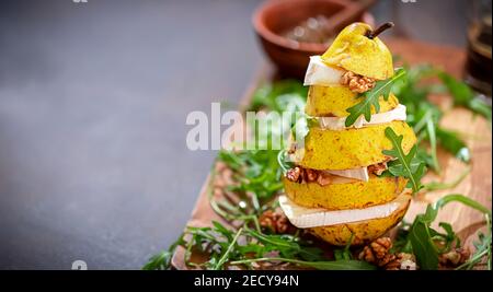 Turmbirne mit Käse, Walnüssen, Rucola, mit Honig auf dunklem Holzhintergrund. Gesundes vegetarisches Essen. Selektiver Fokus Stockfoto