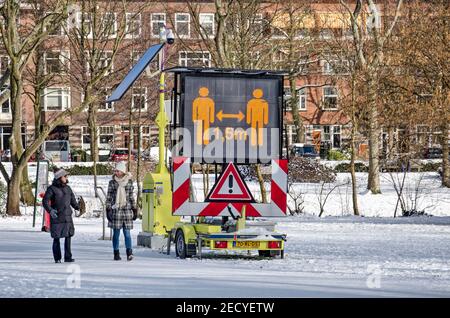 Rotterdam, Niederlande, 10. Februar 2021: Zwei Menschen passieren eine elektronische Matrix Zeichen in Vroesenpark ermutigend halten 1,5 Meter Abstand wie Stockfoto