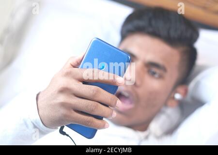 Junger Mann im Bett, der nachts ein Smartphone benutzte Stockfoto
