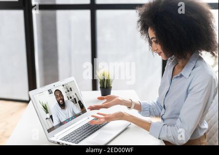 Junge Frau mit lockiger Frisur sitzt am Laptop, im Chat mit Freunden, Kollegen, reden über die Nachrichten, Arbeit, neues Projekt, Arbeit aus dem Büro Stockfoto