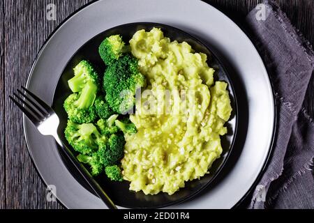 Brokkoli Kartoffelbrei bestreut mit gehackten Mandeln serviert mit gedünsteten Brokkoli-Röschen auf einem schwarzen Teller auf einem dunklen Holztisch, horizontale Ansicht von Stockfoto