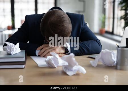 Unglücklicher männlicher Mitarbeiter, der mit der Arbeit im Büro bedrängt war Stockfoto