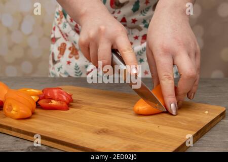 Eine Frau in einer Küche schneidet Orange und Rot Paprika auf einem hölzernen Schneidebrett Hausmannskost Konzept Stockfoto