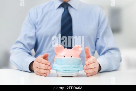 Geschäftsmann hält Sparschwein mit Maske. Finanzielle Probleme von Unternehmern während des Pandemiekonzepts Stockfoto