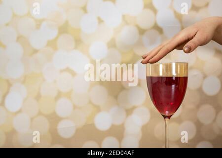 Eine Frauenhand mit langen eleganten Nägeln, die ein Glas halten Von Roséwein auf einem glitzernden goldenen Hintergrund Stockfoto