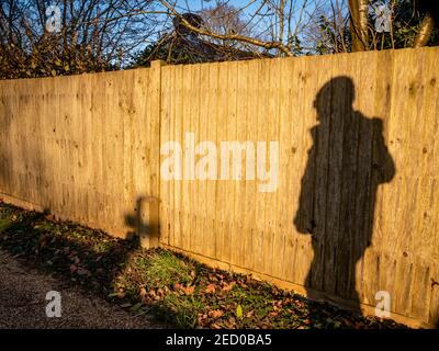 Schattenspaziergänger, der an einem Zaun in der untergehenden Sonne vorbeigeht Stockfoto