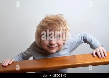 Naughty blonde junge mit über dem Geländer gelehnt und schaut nach unten. Spielen mit Kindern. Stockfoto