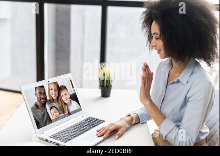 Junge afroamerikanische Geschäftsfrau mit gemischter Rasse, die am Schreibtisch im Büro sitzt und mit Familie chattet, mit Laptop und sozialen Medien telefonieret Stockfoto