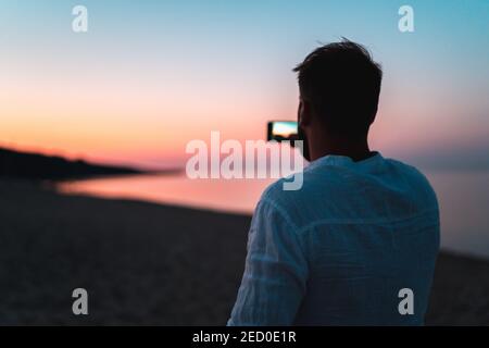 Mann macht Fotos am Strand bei Sonnenuntergang während golden Stunde Stockfoto