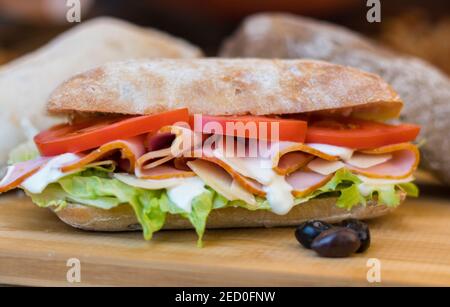 Putenbrötchen und ein dunkles Balkan-Sandwich, mit Sallad, Rucola, Tomaten und Gurkenscheiben, die sich auf einem Holztisch bewegen Stockfoto