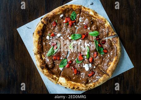 Süße Pizza mit Schokolade, Erdbeeren, Meringues und Minzblättern auf dunkler Holzoberfläche. Bereit zu essen und zu servieren. Stockfoto