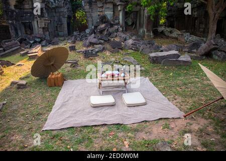 Picknick auf dem Rasen in der antiken Ruine. Japanisches Picknick mit Sonnenschirmen und kleinem Tisch. Romantisches Abendessen im Freien. Antike Tempelruine Dekoration. Honeym Stockfoto