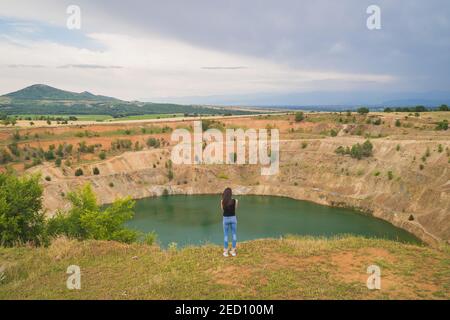 Panoramablick auf junge fit Frau Blick auf große verlassen Kupfermine Grube voller Wasser in Bulgarien Stockfoto