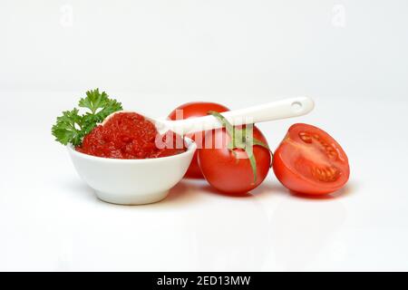 Tomatenmark in Schüssel und Löffel, halbe und ganze Tomaten auf weißem Hintergrund, Deutschland Stockfoto