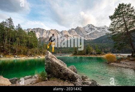 Junger Mann steht auf einem Felsen am Ufer, Blick in die Ferne, Eibsee vor Zugspitzmassiv mit Zugspitze, Wettersteingebirge, in der Nähe Stockfoto