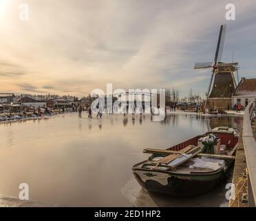 Schipluiden,Holland,14-feb-2021:Leute, die auf dem Kanal in der Nähe der Windmühle Schlittschuhlaufen, es ist vor Jahren so kalt in Holland, dass die Leute Schlittschuhlaufen können Stockfoto