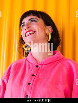 Niedriger Winkel der fröhlichen Weibchen in rosa Kleidung und mit Rote Lippen stehen gegen gelbe Wand im städtischen Bereich und Suchen nach oben Stockfoto