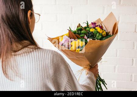 Ernte unkenntlich Person stehend mit Bündel von frischen bunten Blumen Auf dem Hintergrund der weißen Backsteinmauer Stockfoto