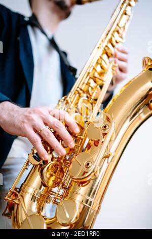 Crop männlichen Musiker spielen Saxophon, während auf weißem Hintergrund Und wegschauen Stockfoto