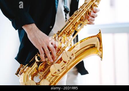 Crop männlichen Musiker spielen Saxophon, während auf weißem Hintergrund Und wegschauen Stockfoto