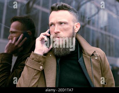 Bärtiger Hipster, der sich an die Wand lehnte und mit ihm redete Ein Telefon Stockfoto
