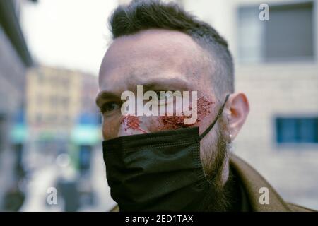 Seitenansicht Hipster Mann mit Bart, Kino Make-up und Maske posiert auf der Straße und Blick auf die Kamera Stockfoto