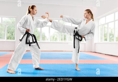 Zwei zielstrebige Frau kämpfen mit Karate-Technik Kick und Punsch in hellen Klasse. Paar fit junge Frauen tragen in weißen Kimono Ausbildung Karate ma Stockfoto