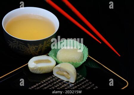 Mochis mit Tee und Essstäbchen, japanischer klebriger Reiskuchen mit grünem Tee-Geschmack, asiatische Süßwarenspezialität Stockfoto