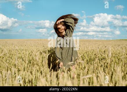 Ähren von Weizen. Junges Mädchen im Kleid zeigt Emotion. Emotional springt und läuft auf einem Sommerfeld mit Stacheletts. Haare fliegen im Wind, Lifestyle Stockfoto