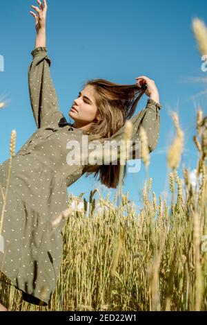 Ähren von Weizen. Junges Mädchen im Kleid zeigt Emotion. Emotional springt und läuft auf einem Sommerfeld mit Stacheletts. Haare fliegen im Wind, Lifestyle Stockfoto