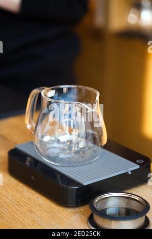 Leerer Glas-Teekanne-Server auf digitaler Waage Nahaufnahme auf Tisch im Café mit Hintergrund verschwommen, niemand Stockfoto