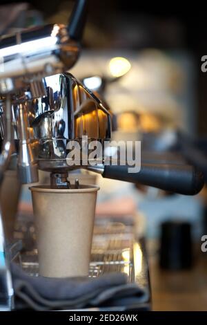 Nahaufnahme von Kaffee Gießen von Ausgießer in Take Away Papiertasse in Espressomaschine Doppelhalter, niemand Stockfoto