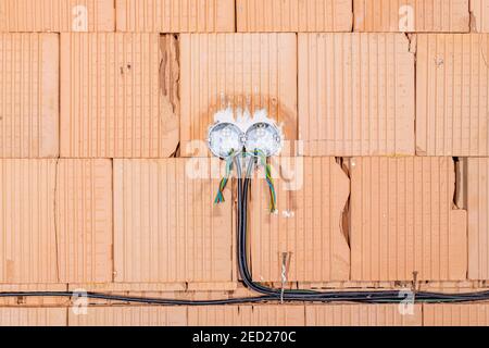 Steckdosenrückwände mit Drähten in einer Wand. Hintergrund der Verkabelung. Bunte elektrische Drähte, die aus der Öffnung der Steckdosen an der Ziegelwand herausragen. Neue Ele Stockfoto