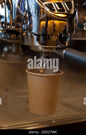 Nahaufnahme von Kaffee Gießen von Ausgießer in Take Away Papiertasse in Espressomaschine Doppelhalter, niemand Stockfoto