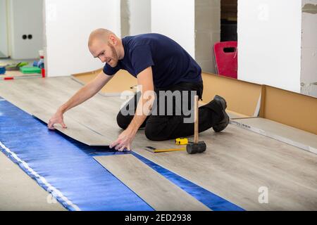 Arbeiter verbinden click Lock Vinyl Bodenplatte Abdeckung zu Hause Renovierung. Mann, der PVC-Boden legt. Handwerker Installation neuer laminierter Holzboden auf blau Stockfoto