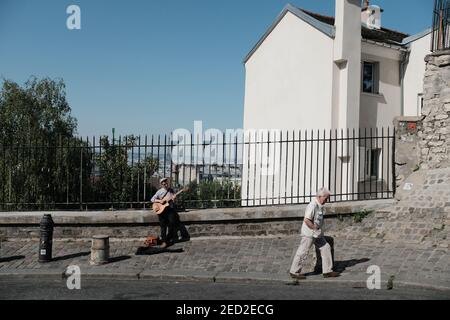 MONTMARTRE, PARIS - 29th. JUNI 2019: Ein älterer Mann, der an einem Musikanten vorbei auf der Rue Saint-Éleuthère in Montmartre vorbeiläuft. Stockfoto