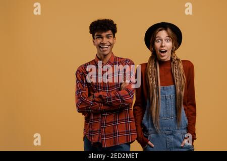 Foto von niedlichen paar Bauern schauen glücklich und überrascht zusammen. Schwarzer Mann trägt kariertes Hemd, weiße Frau trägt Denim-Overall und Hut isoliert braun Stockfoto