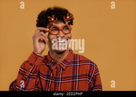 Foto von niedlichen afrikanischen männlichen Landwirt trägt Weihnachtsgläser und lächelt. Der Mann trägt kariertes Hemd, isolierter brauner Hintergrund Stockfoto