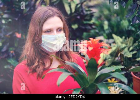 Erwachsene Frau Gärtner in medizinische Maske wählt Bromelia Blumen im Geschäft. Kauf von Zimmerpflanzen für Hausgarten mit Coronavirus Quarantäne Stockfoto