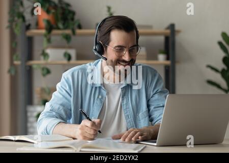 Selbstbewusster junger Mann in Ohrhörern beobachten virtuelle Lektion durch Laptop Stockfoto