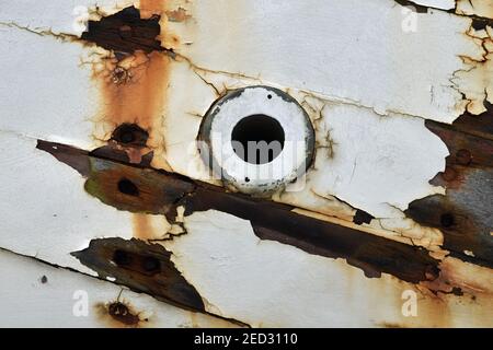 Nahaufnahme Detail des Abschnitts des Bootes Rumpf mit kreisförmigem Loch und extreme Wetterschäden. Rostflecken, Farbe abgeschält von weißen Holzbrettern. Stockfoto
