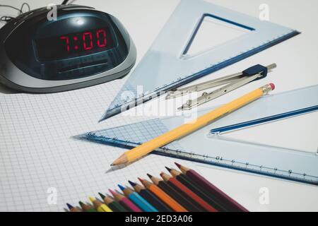 Ein Wecker zeigt 7 Uhr an, um zur Schule zu gehen, ein Kompass, ein Bleistift und Zeichenbretter sind in der Nähe platziert. Stockfoto