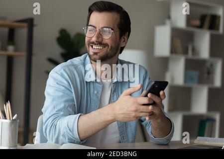 Junger Mann, der Zelle hält, schaut weg aufgeregt mit neuer Gelegenheit Stockfoto