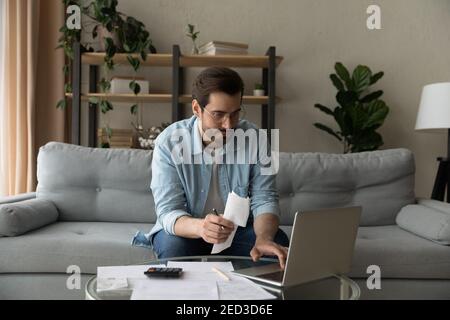 Serious Millennial männlich konzentrierte sich auf die Zahlung von Stromrechnungen mit Laptop Stockfoto