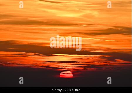 Eine Nahaufnahme der untergehenden Sonne teilweise hinter Wolken Stockfoto