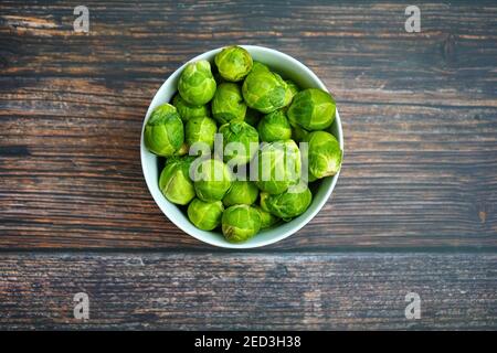 Eine weiße Schale mit rohen Rosenkohl auf einem rustikalen Holztisch. Stockfoto