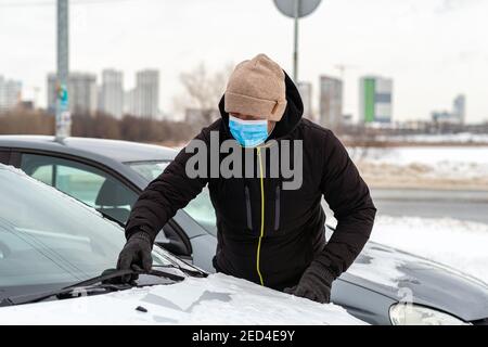 Mann in einer Schutzmaske Reinigung Auto Windschutzscheibe von Schnee. Stockfoto