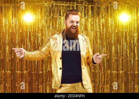 Ungehemmter bärtiger Mann in glänzendem goldenem Anzug tanzend und habend Spaß bei der Diskoparty Stockfoto